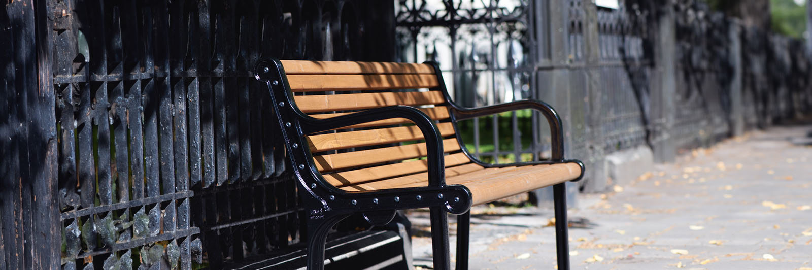 Close up of a wooden park bench with black steel frame and armrests on a side of a walkway.